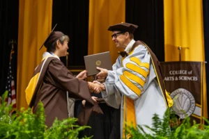 A Valpo graduate shakes hands with a faculty member while receiving a diploma, ready to meet the needs of the world at a graduation ceremony.