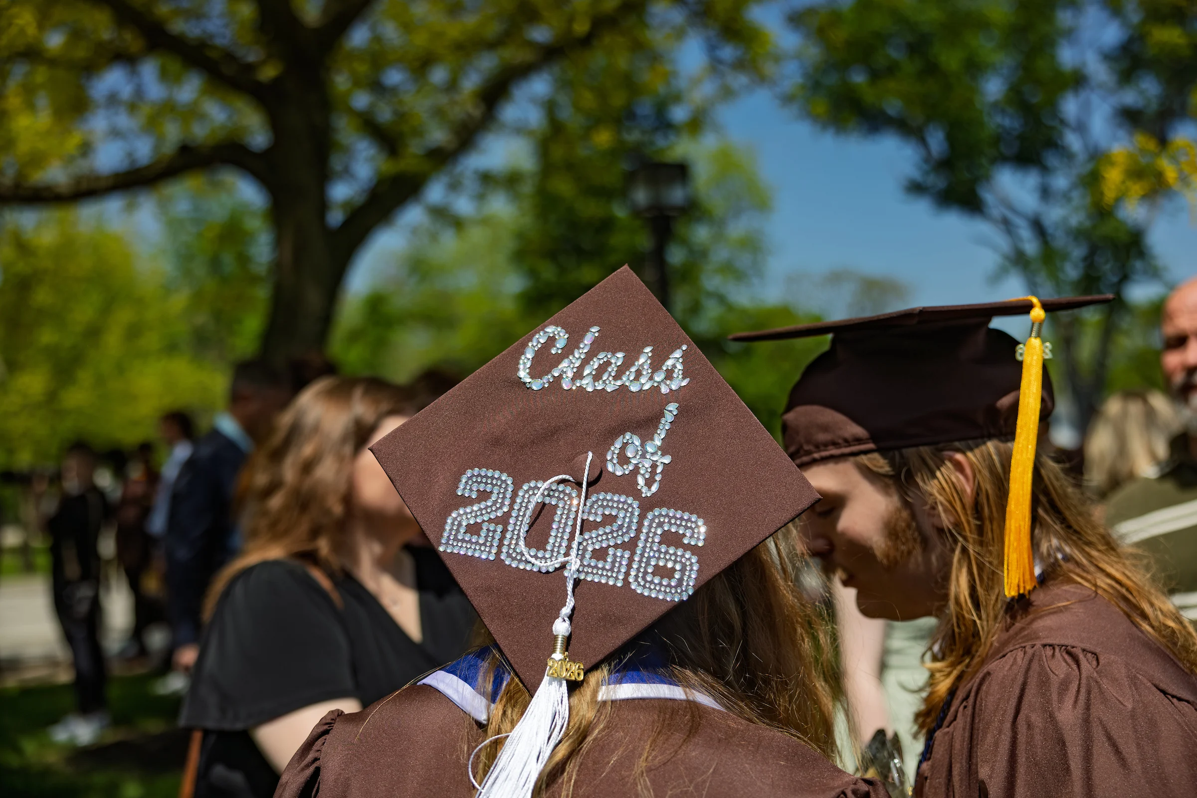 A graduate from Valparaiso University wears a decorated cap reading "Class of 2026" while celebrating with the graduating class at an outdoor ceremony.
