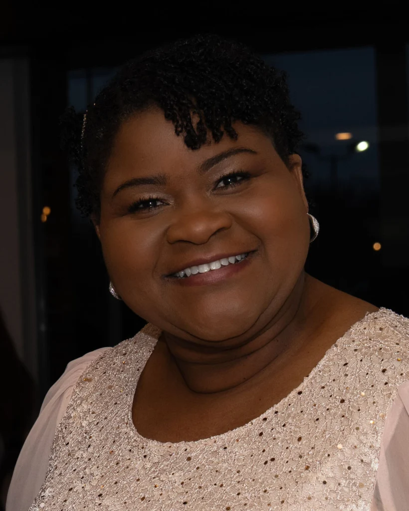 Smiling woman with short curly hair, wearing a sparkly light-colored top, poses indoors—proud participant in Student Research at Valparaiso University.