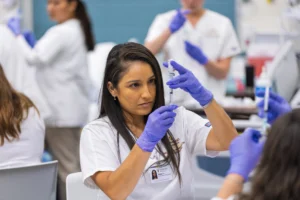 A Valparaiso University accelerated nursing student wearing white scrubs and purple gloves prepares a syringe in a simulation lab.