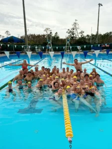 A large group of swimmers, including up-and-coming career hopeful Ricky Helmboldt, pose together in an outdoor pool, smiling and wearing swim caps and goggles.