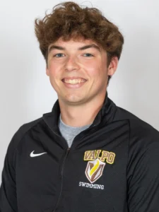 Young man smiling, wearing a black Valpo Swimming jacket with a white background—Ricky Helmboldt showcases his up-and-coming career potential.