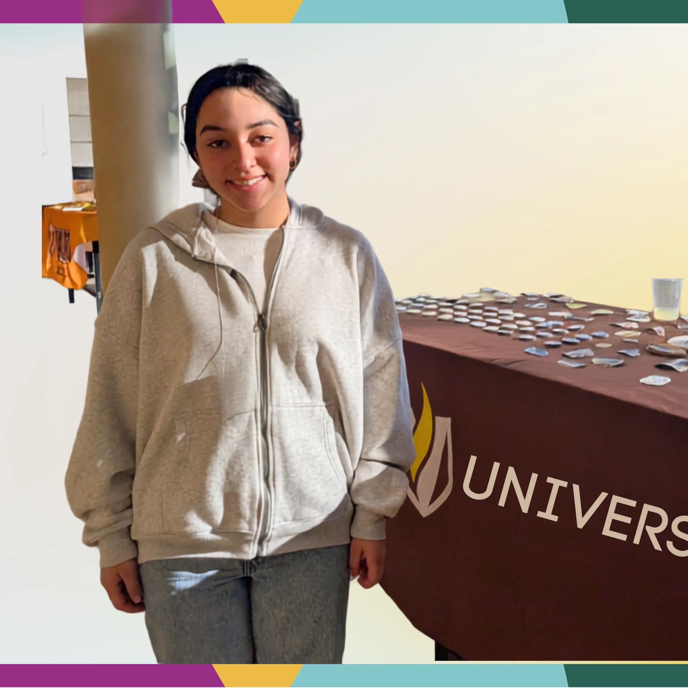 A person in a gray hoodie stands by a table with name tags and a "UNIVERS" logo, highlighting the event's multicultural spotlight.