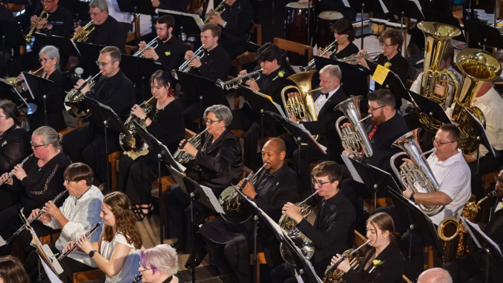 A large concert band, honoring the Sousa Legacy, plays wind and brass instruments while seated in rows during a performance.
