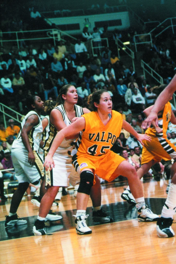 A women’s basketball game with players in action, including Jeanette Gray, M.Ed., in a yellow "VALPO 45" jersey defending for the Beacons.