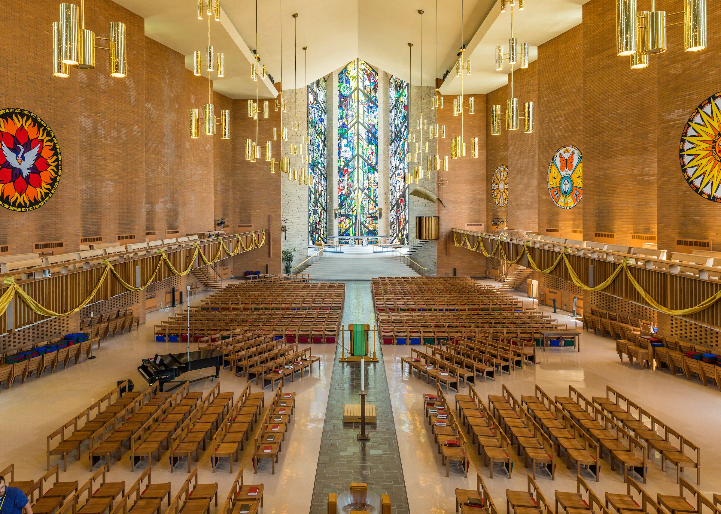 Large church interior set for Morning Prayer, with rows of wooden chairs, stained glass windows, and colorful wall art.