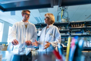 Two scientists in lab coats discuss research in a bright laboratory, highlighting the importance of professional growth and the opportunity to find a mentor in such an inspiring environment.