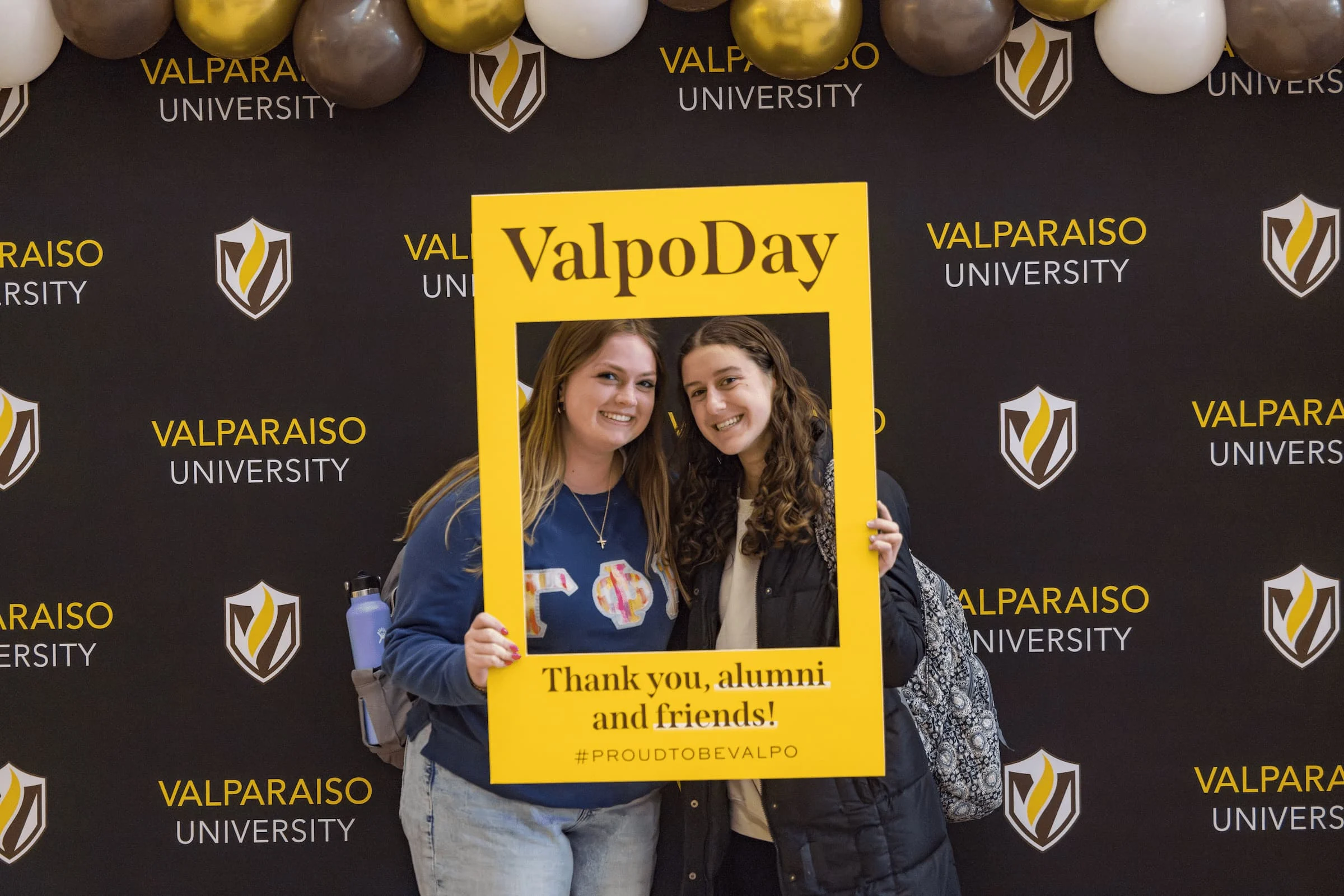 Two women smile holding a yellow "ValpoDay" frame—one of the event's fun photo templates—in front of a Valparaiso University backdrop.