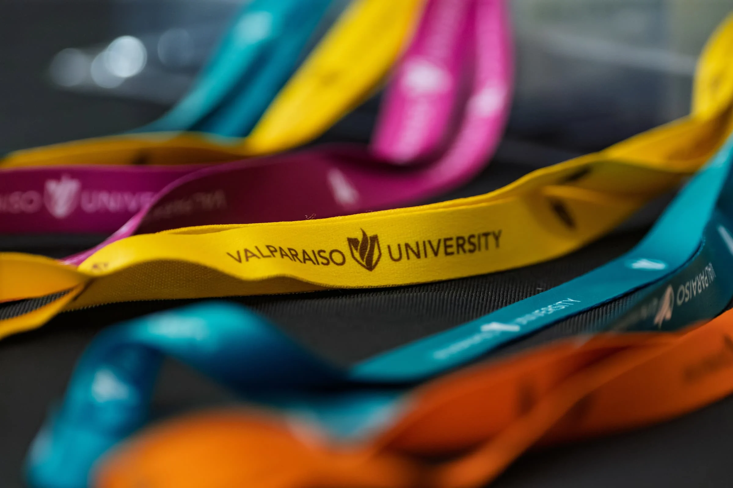 Colorful lanyards, including a yellow one labeled "Valparaiso University," are spread out on a surface next to templates for personalized designs.