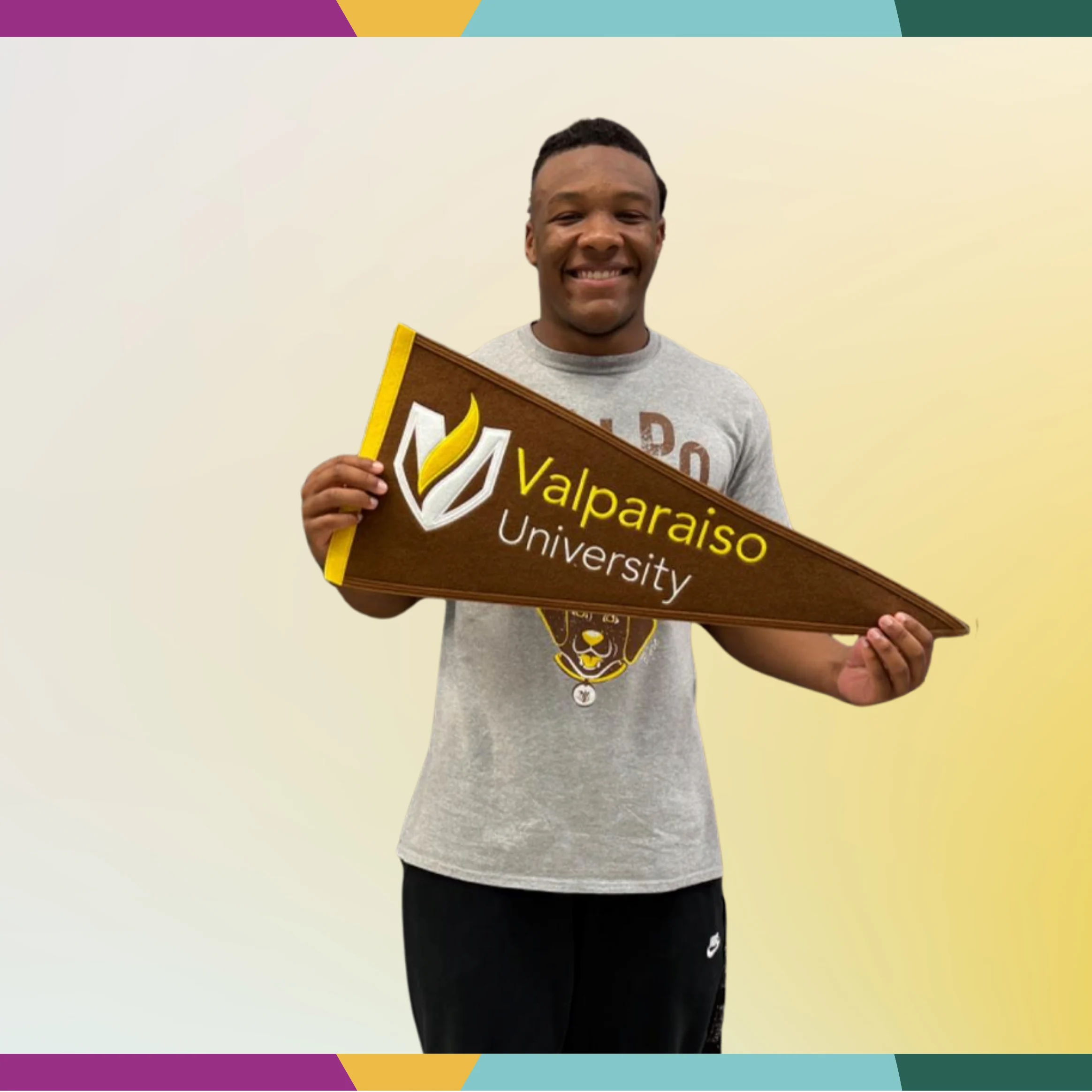 Smiling multicultural student holding a Valparaiso University pennant against a light gradient background with a colorful border, in the spotlight.