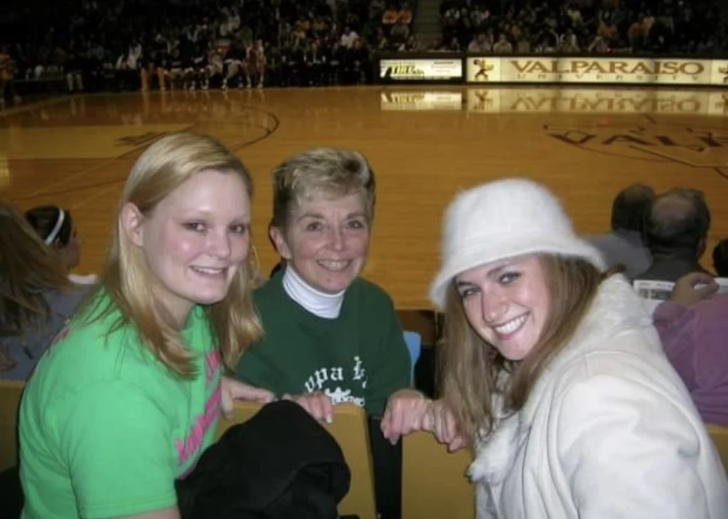 Meteorologist Meredith Garofalo and two friends are smiling courtside at a basketball game in an indoor Beacon arena.