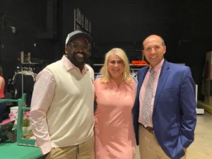 Three people, including Aaron Willis, smiling and posing together indoors, dressed in business casual and formal attire.