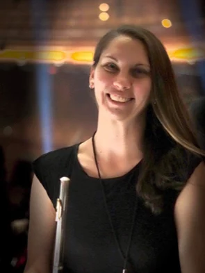Erica Sipich beams in a black dress, smiling and holding a flute, with blurred lights in the background—a true beacon of elegance.