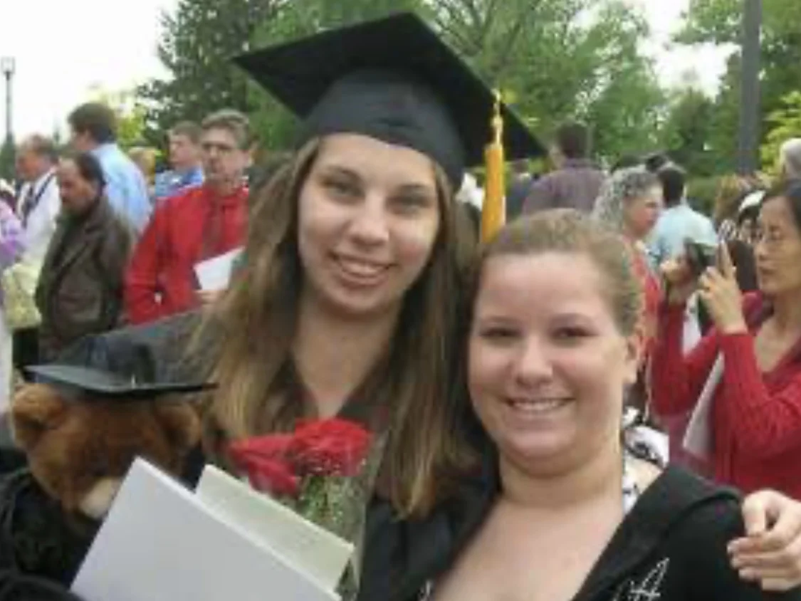 Two women smiling at a graduation ceremony, one in a cap and gown holding flowers and documents, celebrate with Erica Sipich at Beacon.