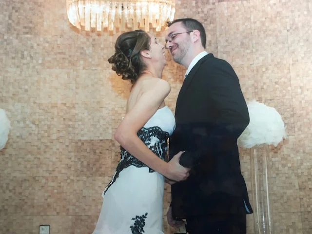 Erica Sipich and Huffstodt, dressed formally, smile closely together in front of a textured wall and chandelier at Beacon.