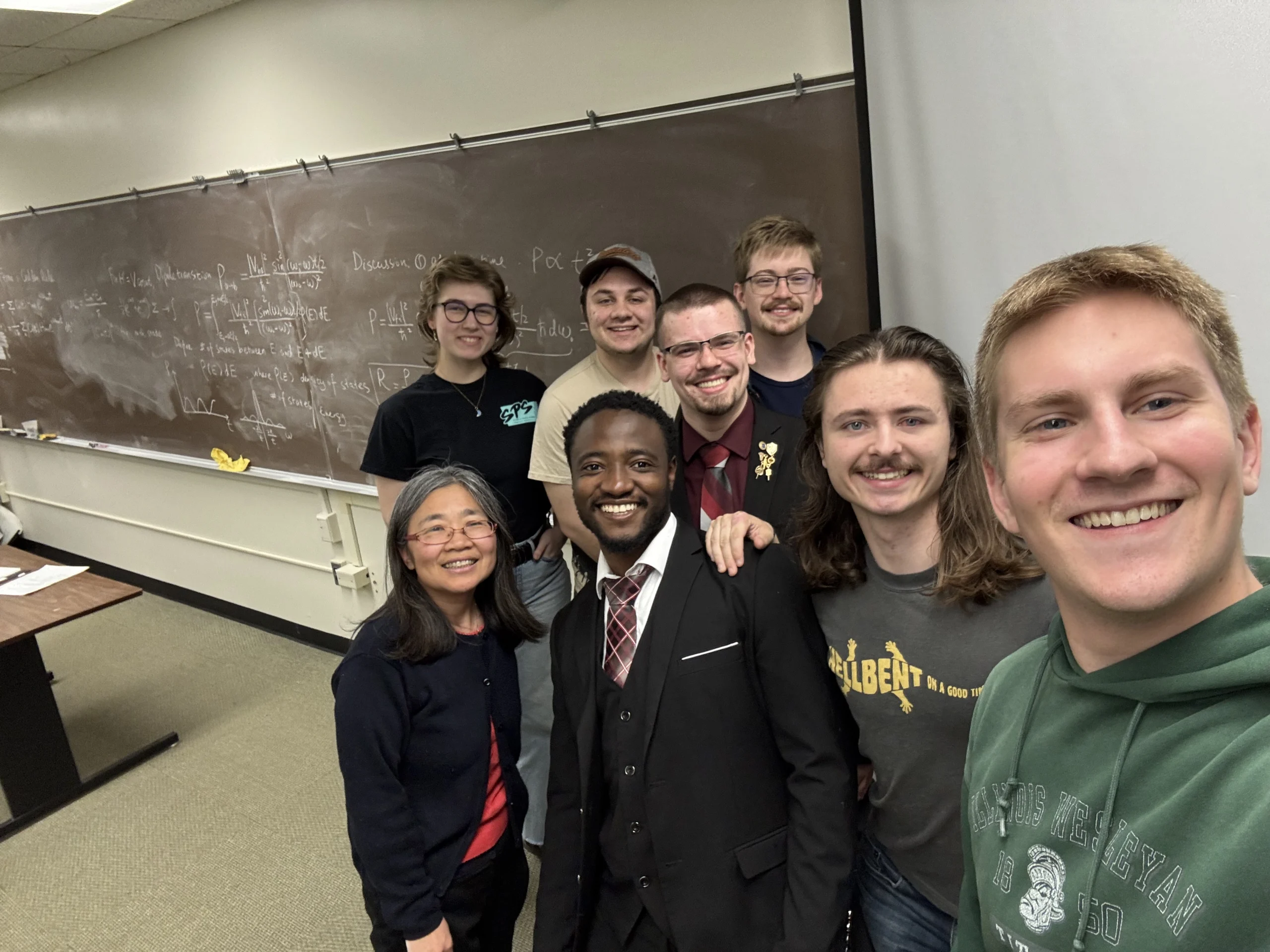 A group of seven people, including International Alumni, smiling and posing together in a classroom in front of a chalkboard at Valparaiso University.