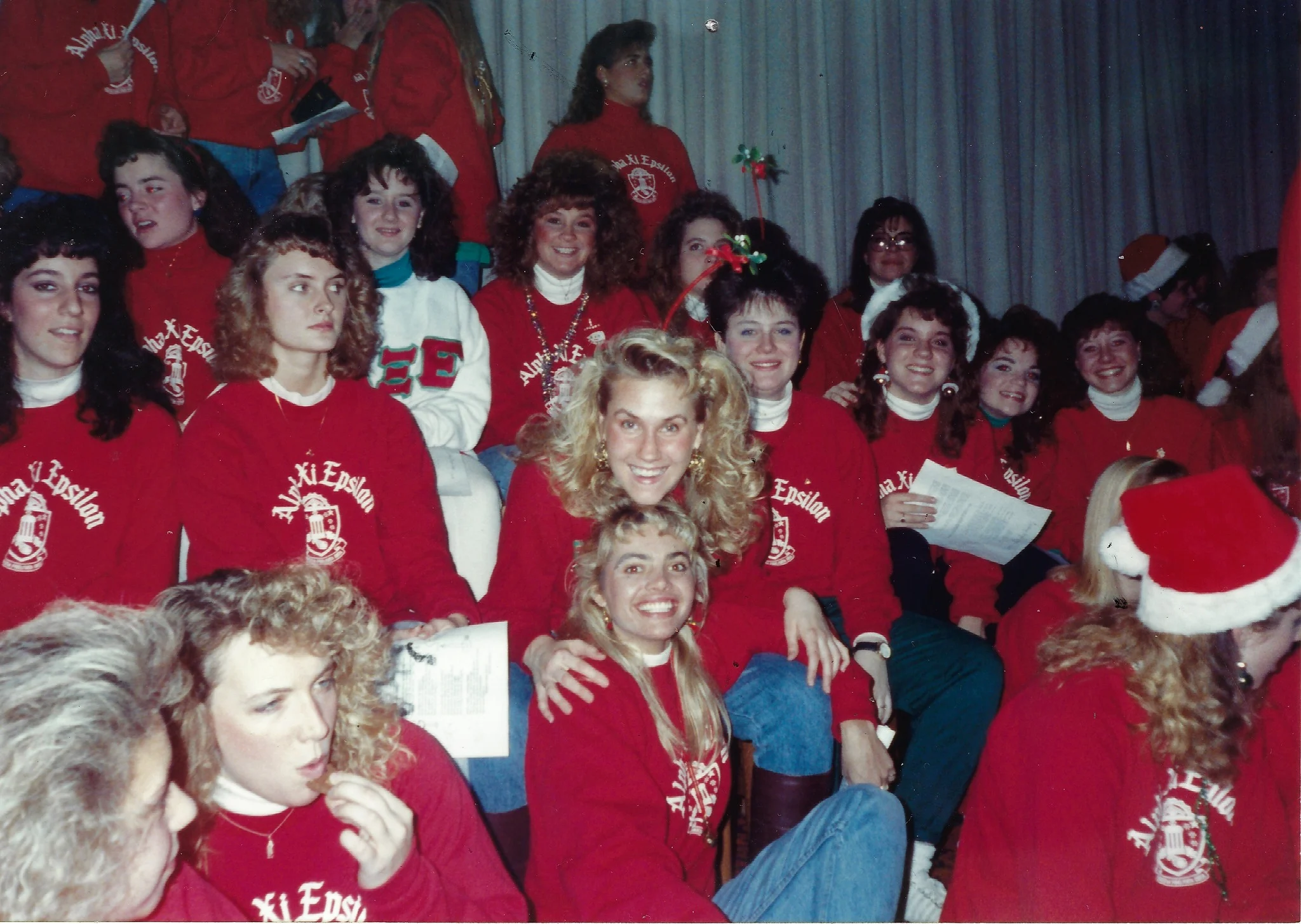 Group of young women in red Alpha Xi Delta shirts sitting together and smiling at an indoor Beacon event.