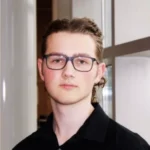 Young person with glasses and long hair, wearing a black shirt, standing indoors near a white wall—ready for another LINC Language Tutoring session.