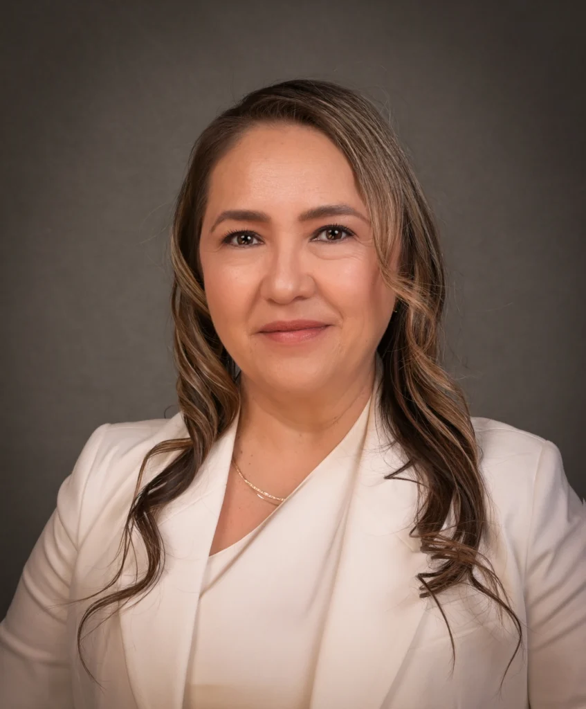 Woman with wavy light brown hair in a white blazer, smiling in front of a plain gray background, representing Veteran Student Services.