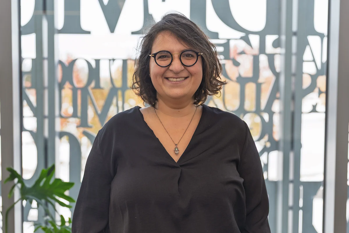 Professor Margarita Rayzberg, a woman with glasses and short dark hair, smiles in front of a window with decorative lettering—a moment that reflects her connection to family immigration and the Indiana Jewish Historical Society.