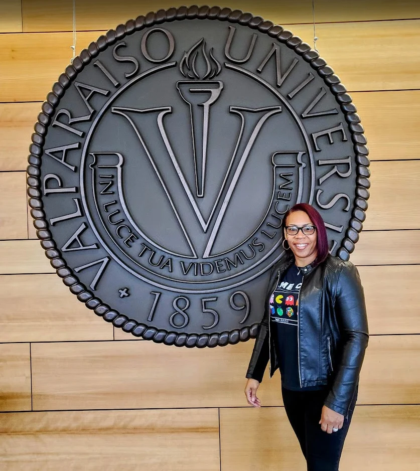 Shantée Lewis stands and smiles in front of a large Valparaiso University seal on a wood-paneled wall, embodying the spirit of the Beacon.