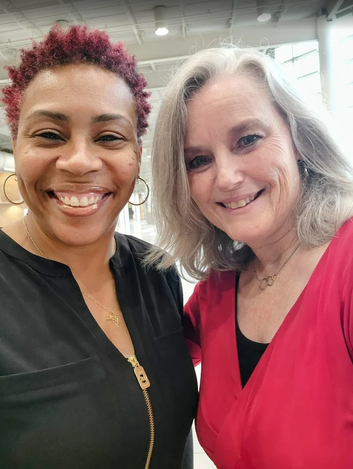 Two women smiling together indoors, one with short curly hair and the other with long gray hair, capture a joyful moment at Beacon in 2022, reflecting the vibrant spirit of Shantée Lewis’s community events.