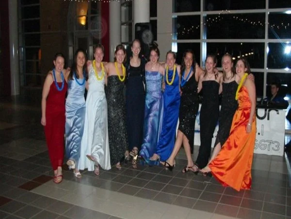 A group of women in formal dresses pose together indoors, smiling with their arms around each other at the Johnson MEM event.