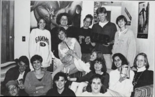 A group of smiling young people pose together in a casual living room setting, with a Beacon lamp softly illuminating the scene.
