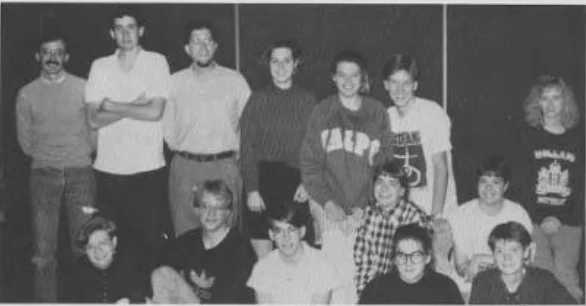 A group of sixteen people pose together indoors, smiling and wearing casual clothes, with Chris Hanson at the center serving as a beacon of warmth and camaraderie.