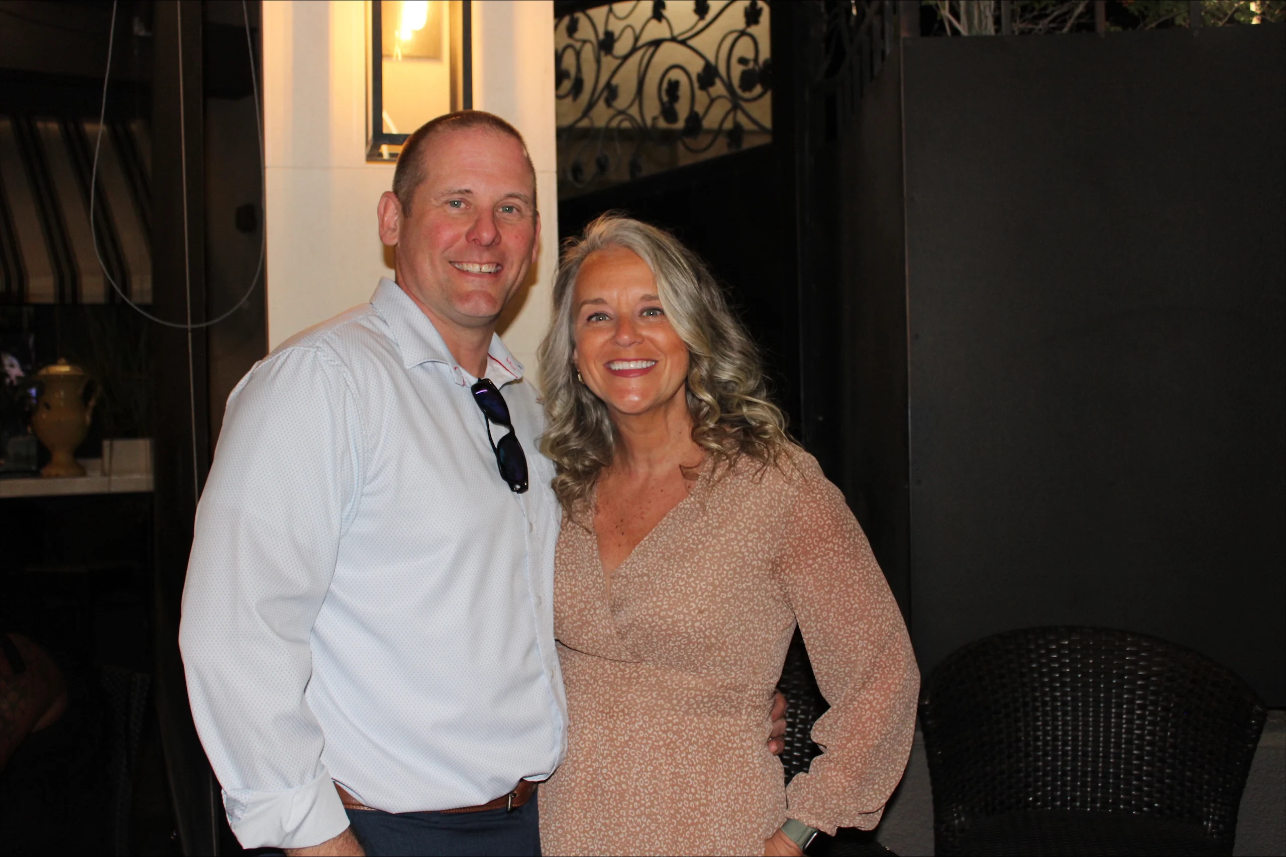Smiling man and woman, Katie Adrian and Jasnieski, pose together indoors in semiformal attire, with Beacon’s dark background elements adding depth to the scene.