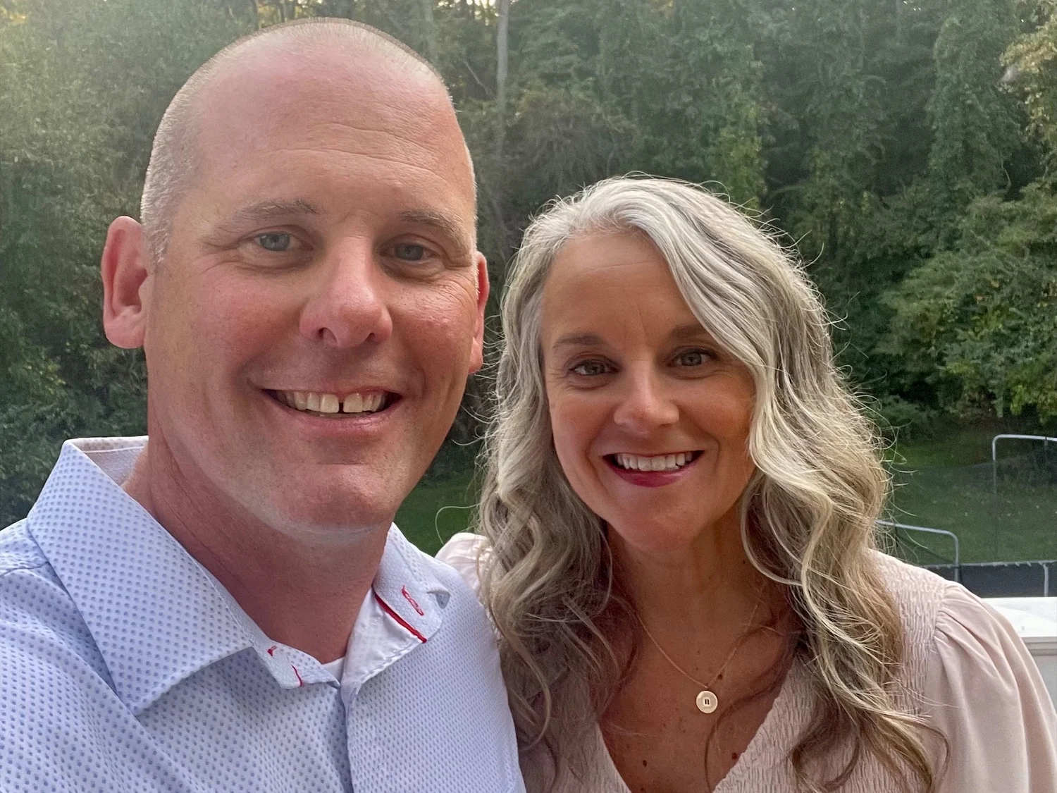 A smiling man and woman, Jasnieski and Katie Adrian, pose together outside with trees in the background.