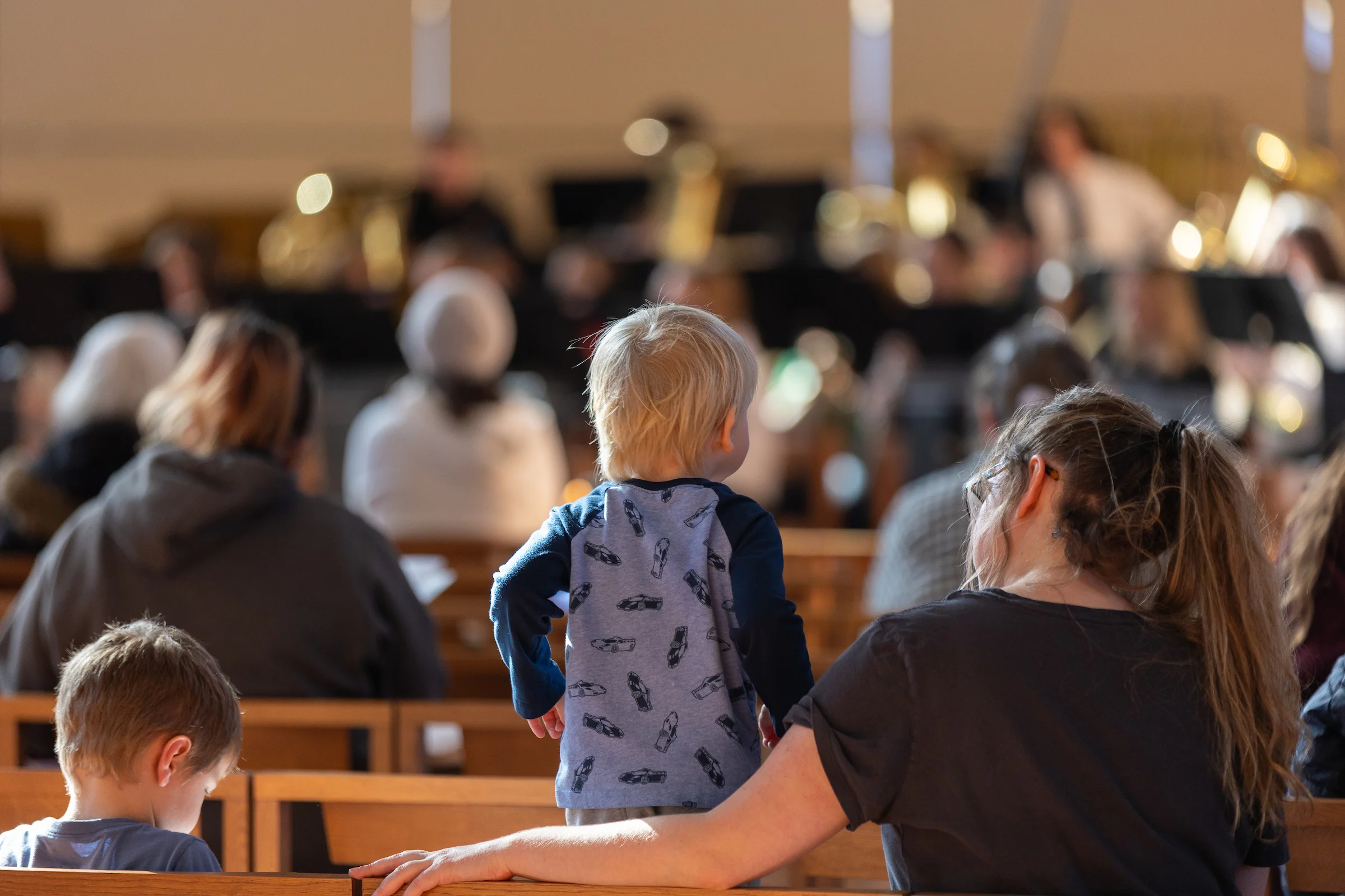 A young child stands on a pew beside a woman, watching a performance at Valparaiso University’s Lullaby Project in a crowded hall.