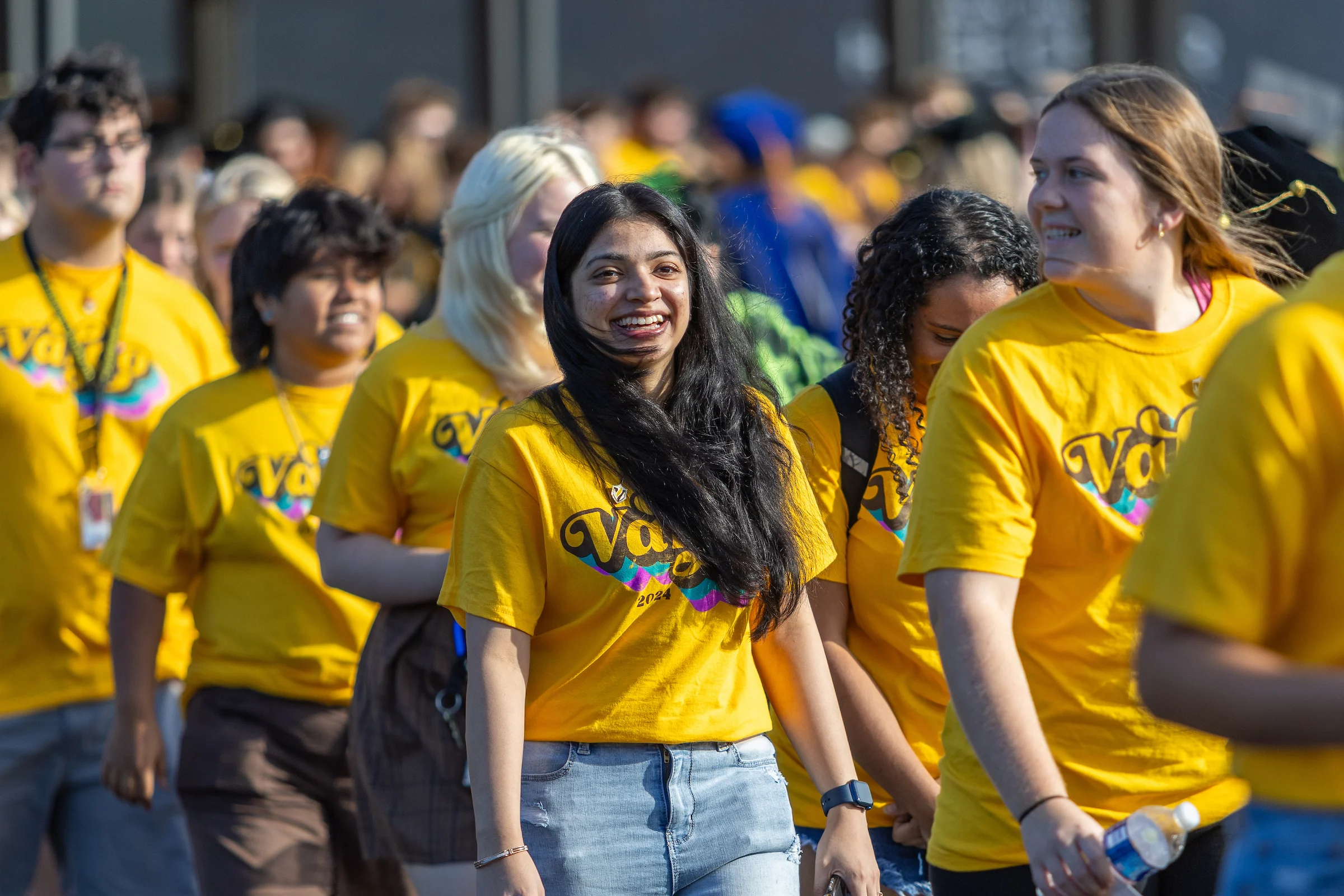 A group of people in yellow shirts smiles while walking together outside during the day, showcasing the spirit of student organizations and student activities.