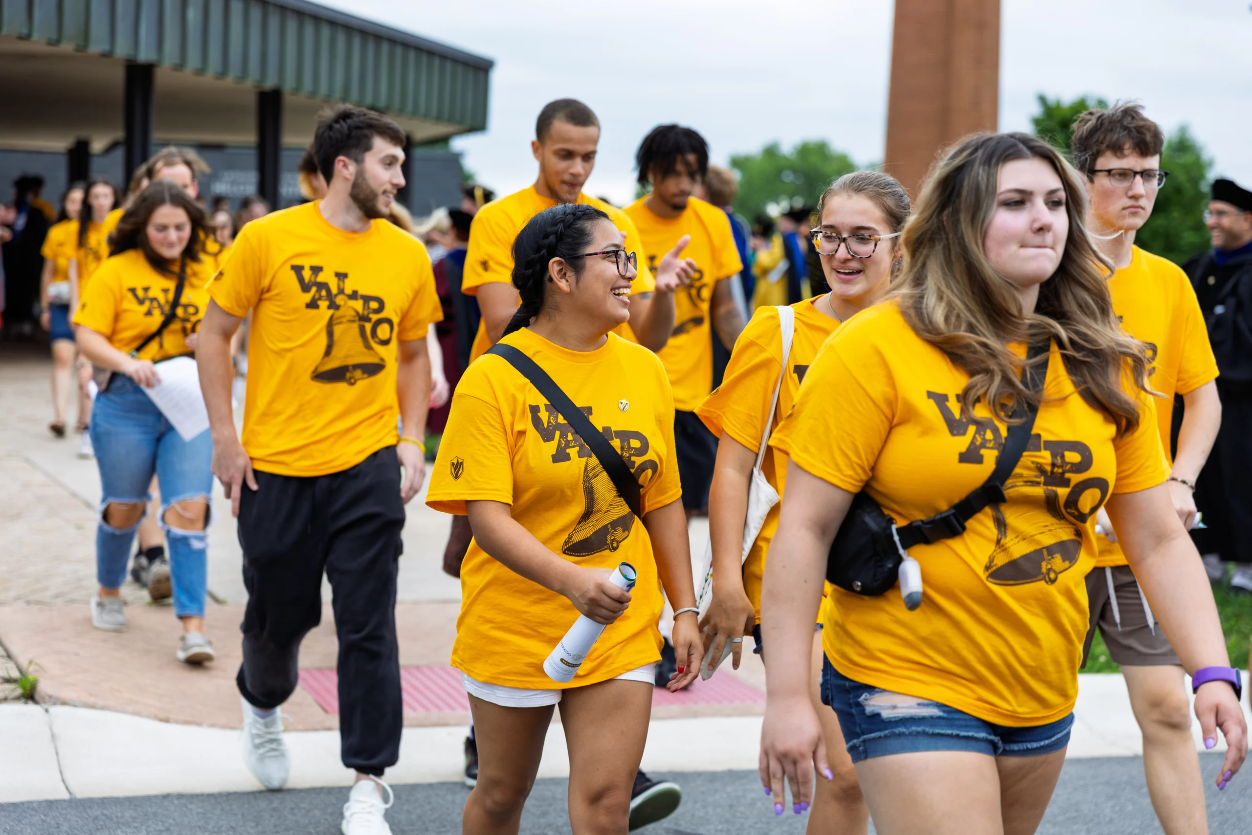 Group of students in matching yellow shirts walk and talk outside on campus during Welcome Week, some holding papers.