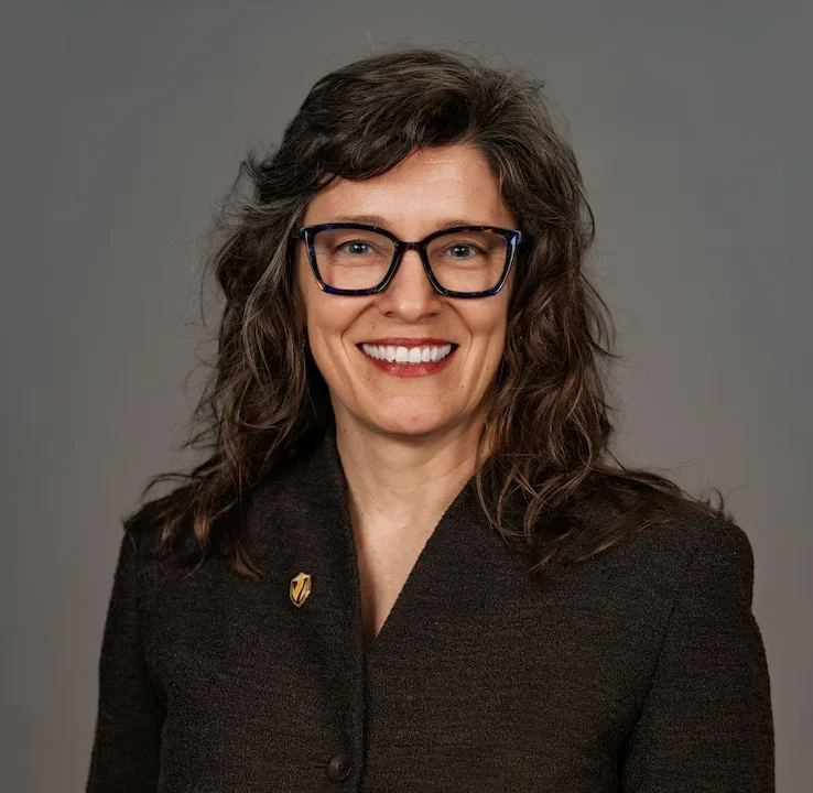 Dr. Nicole Smith, a woman with dark curly hair and glasses, wearing a dark blazer.