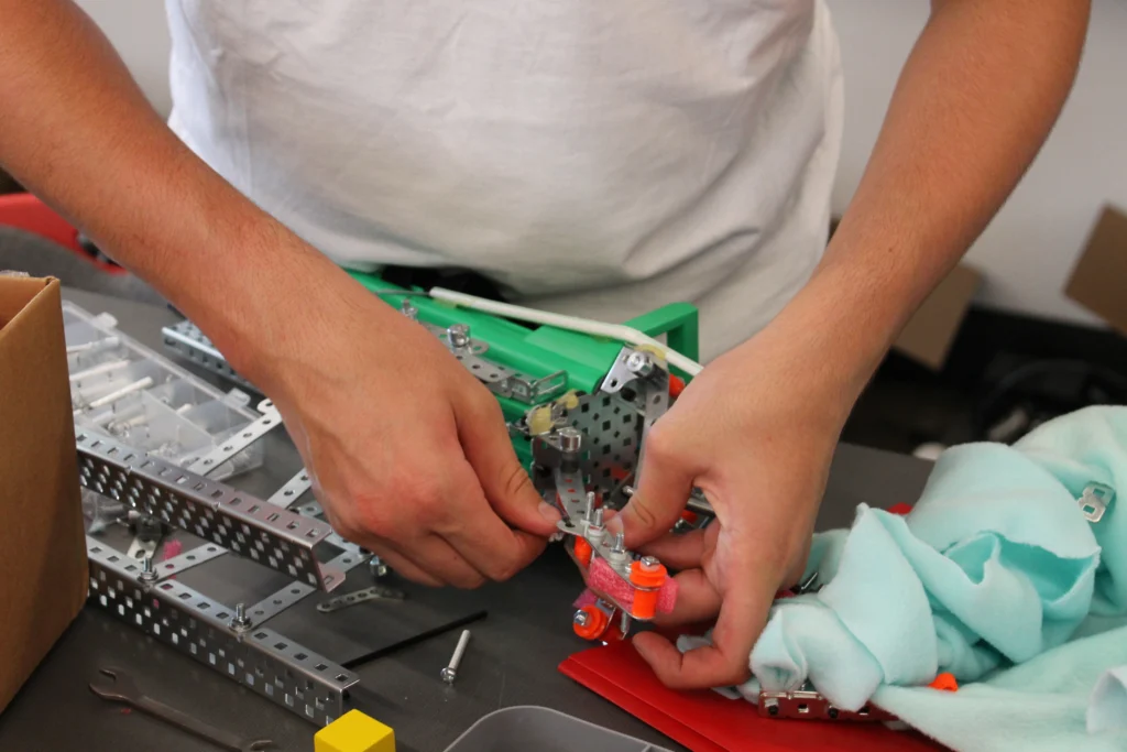 Hands assembling metal and plastic robotics parts on a table with tools and fabric nearby, as high school students from Valparaiso University’s Beacon Academy Engineering Camp collaborate on their latest project.