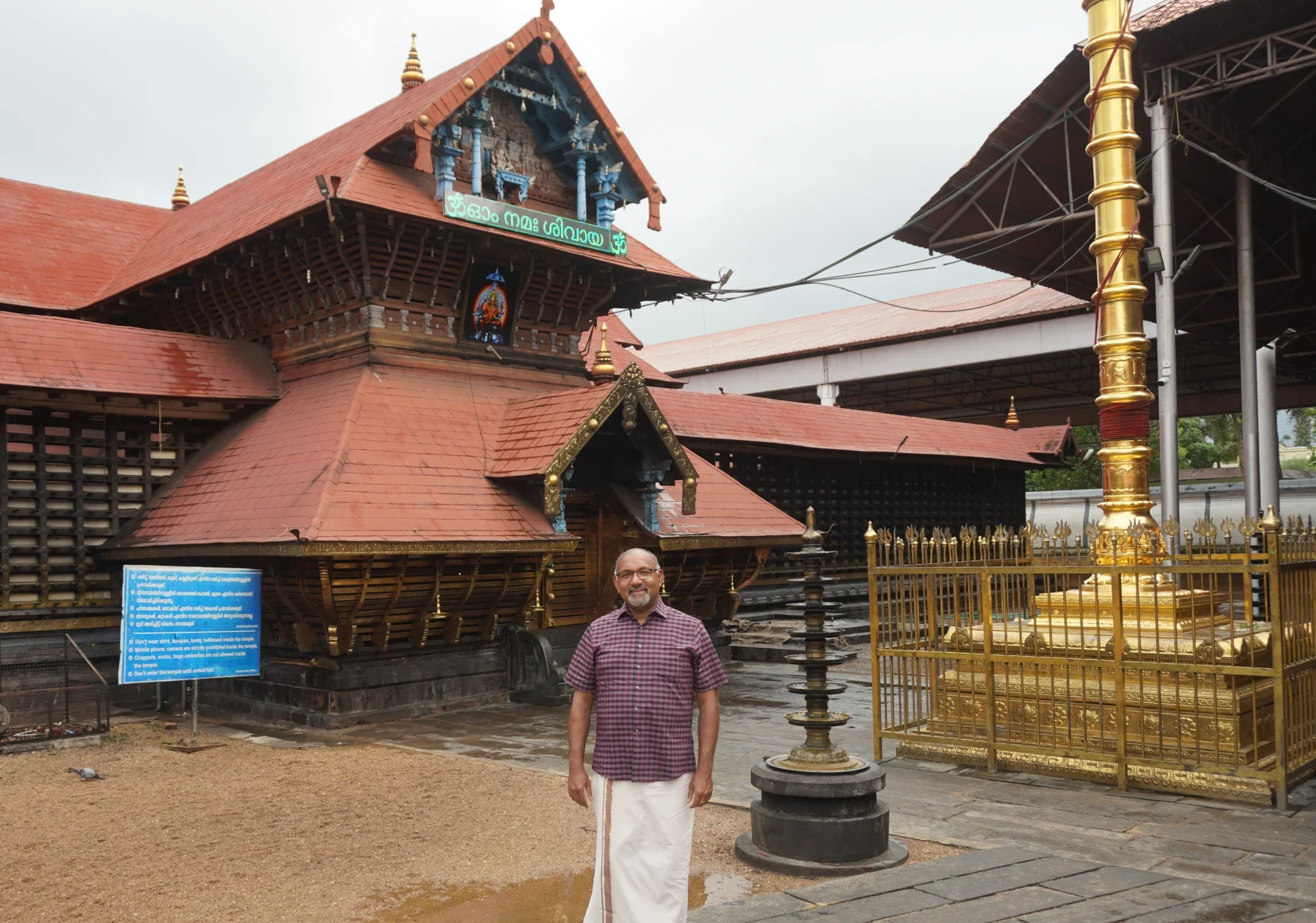 A man in traditional attire stands in front of a South Indian temple with red roofs and golden pillars, embodying the spirit captured by ethnographer George Pati in his Valpo studies.