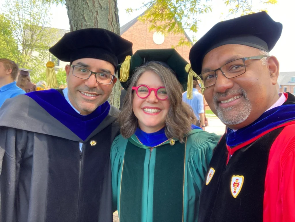 Three smiling people in academic regalia, including ethnographer Professor George Pati, pose outdoors at a Valpo graduation ceremony.