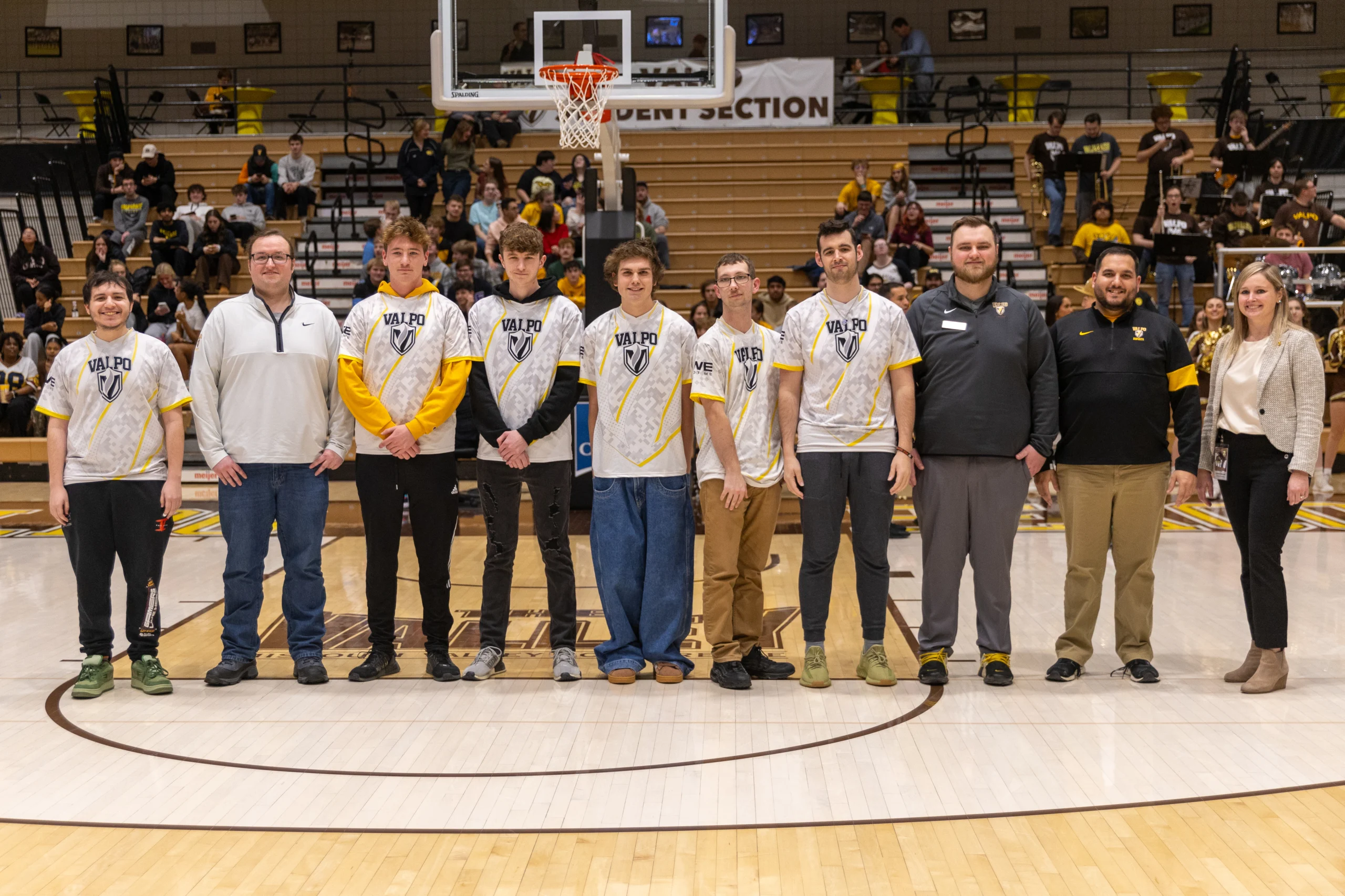 Ten people stand in a row on a basketball court, some wearing matching sports jerseys, posing for a photo that captures the spirit of teamwork—whether on the hardwood or in the world of esports.