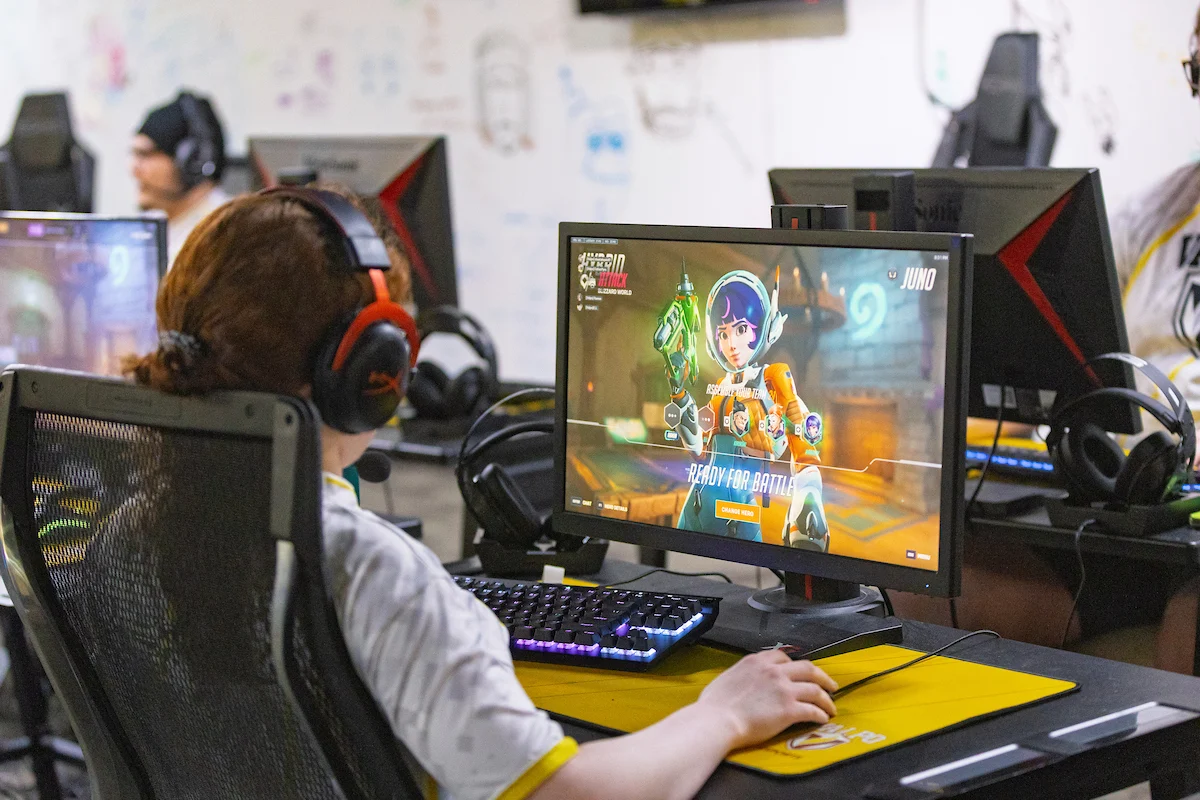 A person is playing a video game on a desktop computer in an esports gaming center, with teammates nearby competing in the lively esports atmosphere.