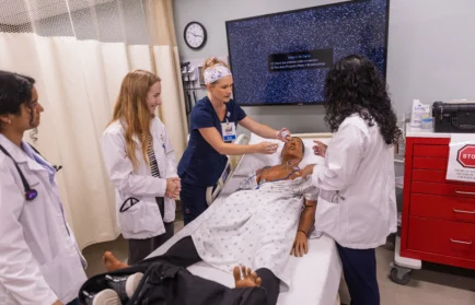 Four health professions students practice a procedure on a mannequin in a clinical training room, demonstrating the collaborative spirit fostered by the CASS community for health professions students.
