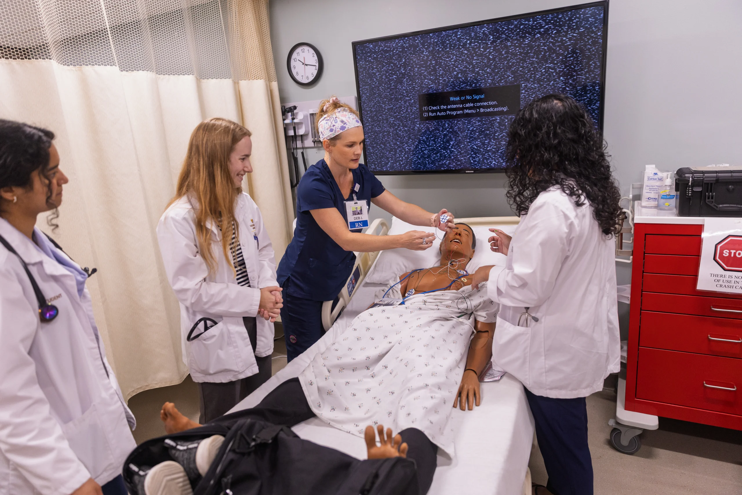 Four health professions students practice a procedure on a mannequin in a clinical training room, demonstrating the collaborative spirit fostered by the CASS community for health professions students.