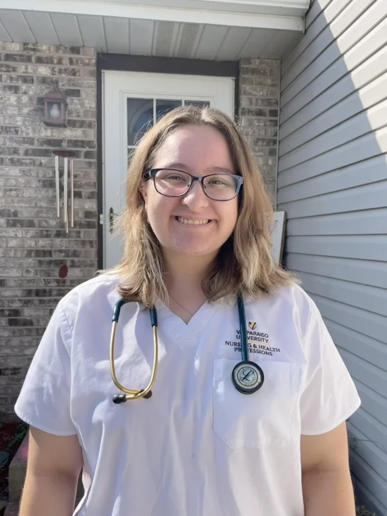 A woman in glasses and a white nurse uniform, smiling outside with a stethoscope around her neck, represents the vibrant community for health professions students at CASS.