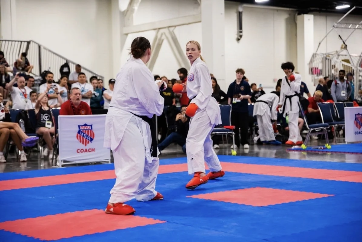 Two karate athletes spar in a competition, watched by an audience and officials in a gymnasium setting, as Valpo’s own World Champion Hailey Reichelt showcases her impressive skills.