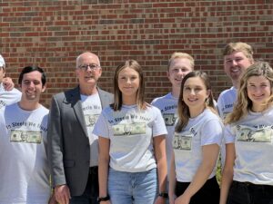 Group of people in matching “In Steele We Trust” shirts standing in front of a brick wall, smiling at the camera—members of Valparaiso University’s renowned Student-Run Investment Portfolio managing over $1 Million.