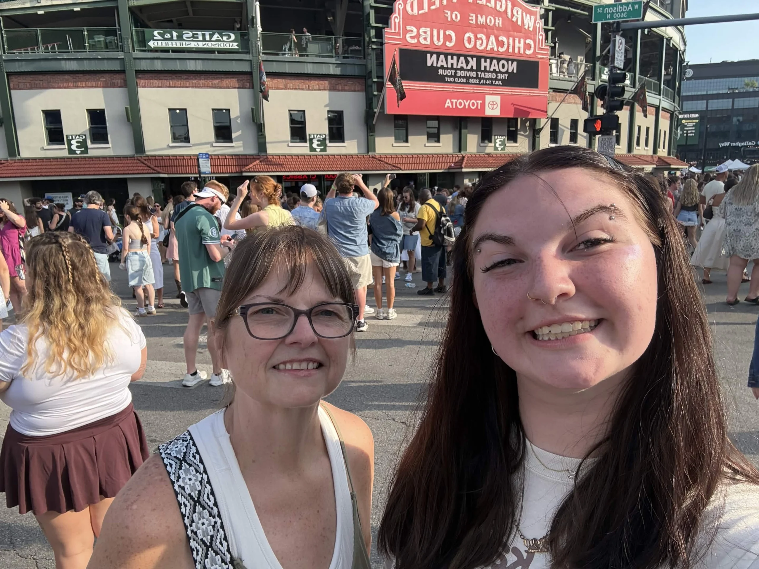 Two women smile for a selfie outside a stadium with a crowd and marquee visible in the background, capturing the excitement of the UPC event.