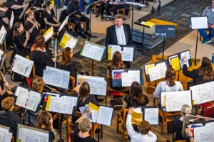 A conductor leads an orchestra of musicians playing various instruments with sheet music in a bright room, capturing the vibrant spirit of the Fall Arts season at Valpo.
