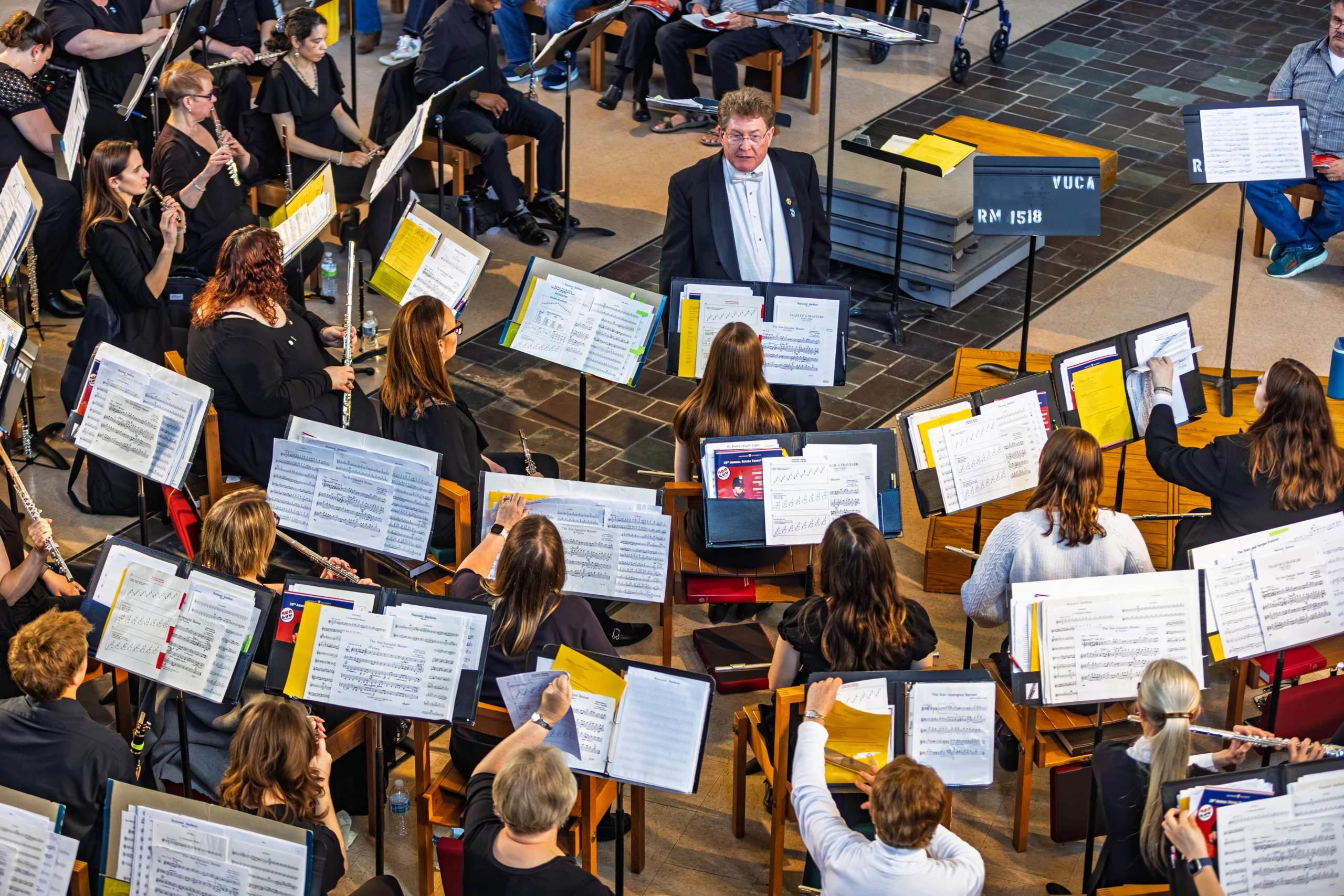 A conductor leads an orchestra of musicians playing various instruments with sheet music in a bright room, capturing the vibrant spirit of the Fall Arts season at Valpo.