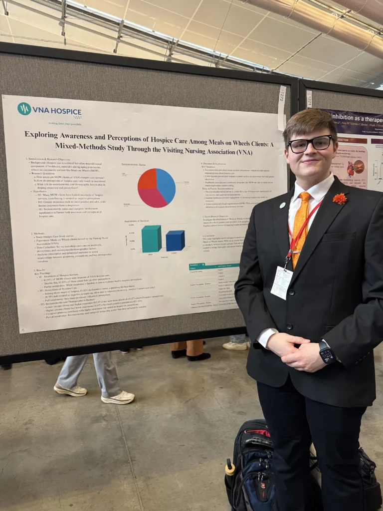 A person in a suit stands by a research poster with charts at a conference or academic event, showcasing findings on community well-being and its impact on healthcare leadership.
