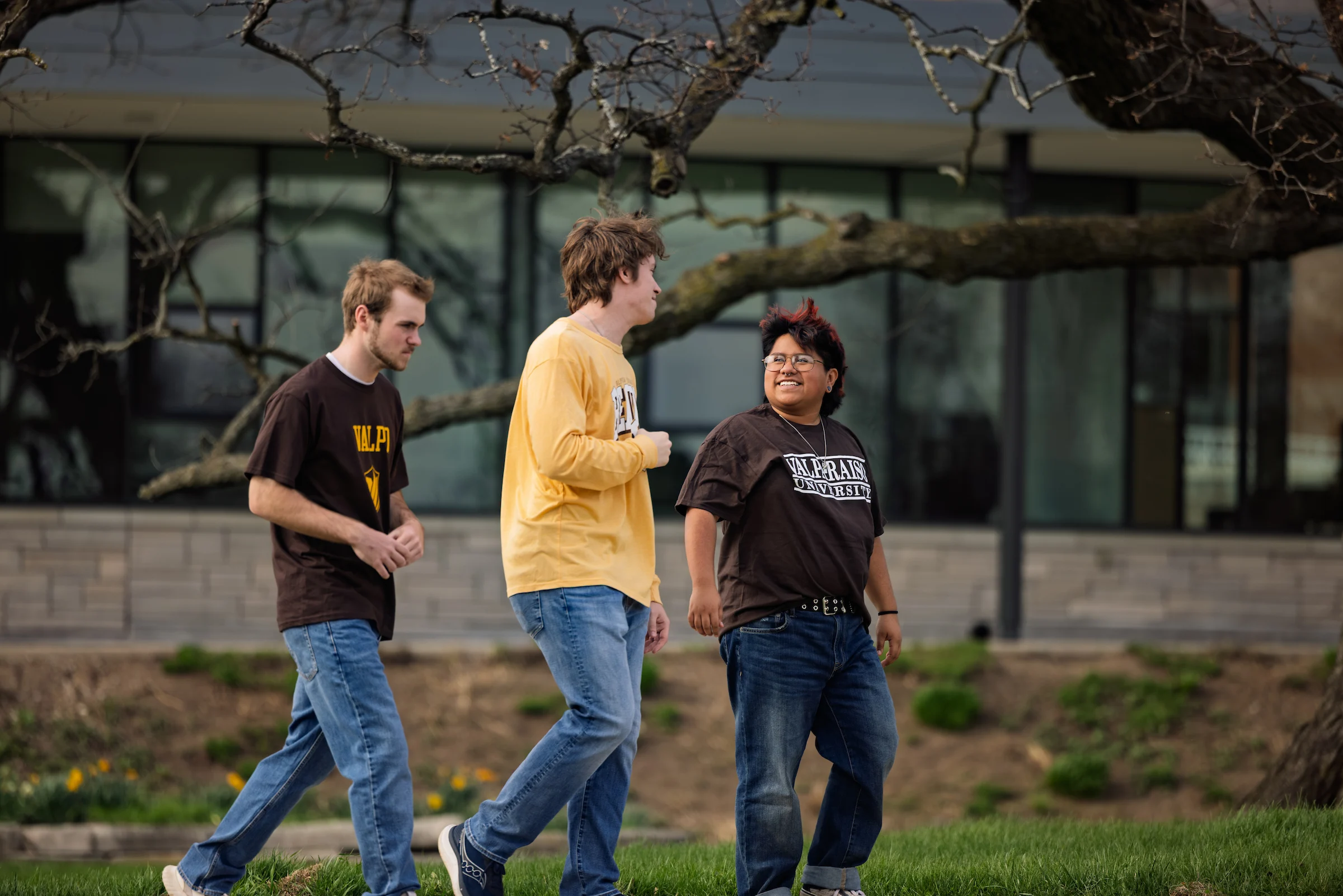 Three people walk together outside, talking and smiling, with trees and a modern building in the background—capturing the spirit of the Educating Character Initiative at Valparaiso University.